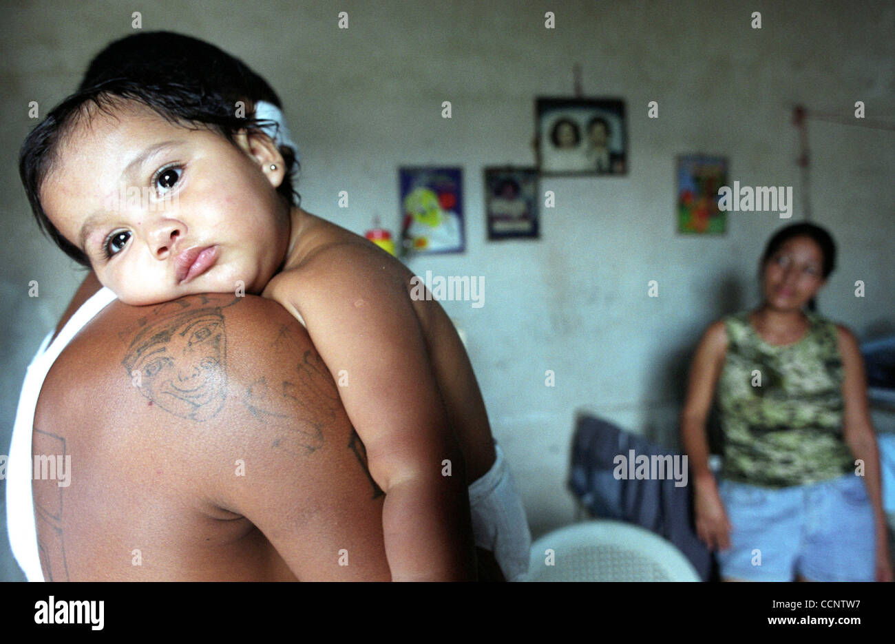 Former Mara Salvatrucha 13 gang member Christian Antunez, 23, hugs his 18-month-old daughter, Jeslin, in the room he shares with his wife, Angelina Matta in San Pedro Sula, Honduras.  Photographer:  Luis J. Jimenez City: San Pedro Sula Country: Honduras Date: June 10, 2004 Stock Photo
