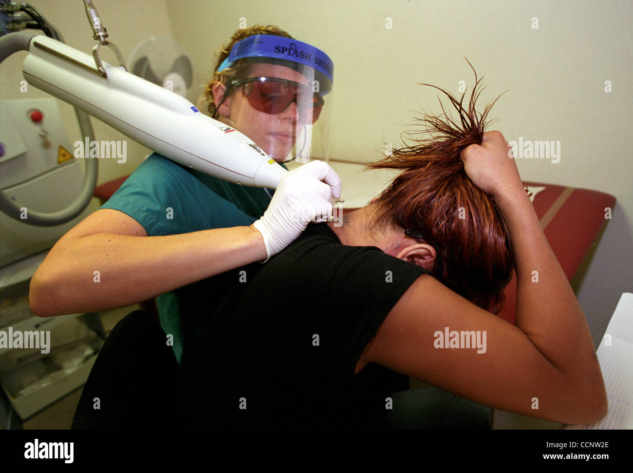 At the Sunrise Outreach Clinic in Los Angeles, Ca., Nurse Allison Curtis (background) uses a laser to remove a tattoo from the neck of Evelyn, (foreground) who is a former member of the 18th Street gang.   Photographer: Luis J. Jimenez City: Los angeles State: California Country: USA Date: July 20,  Stock Photo