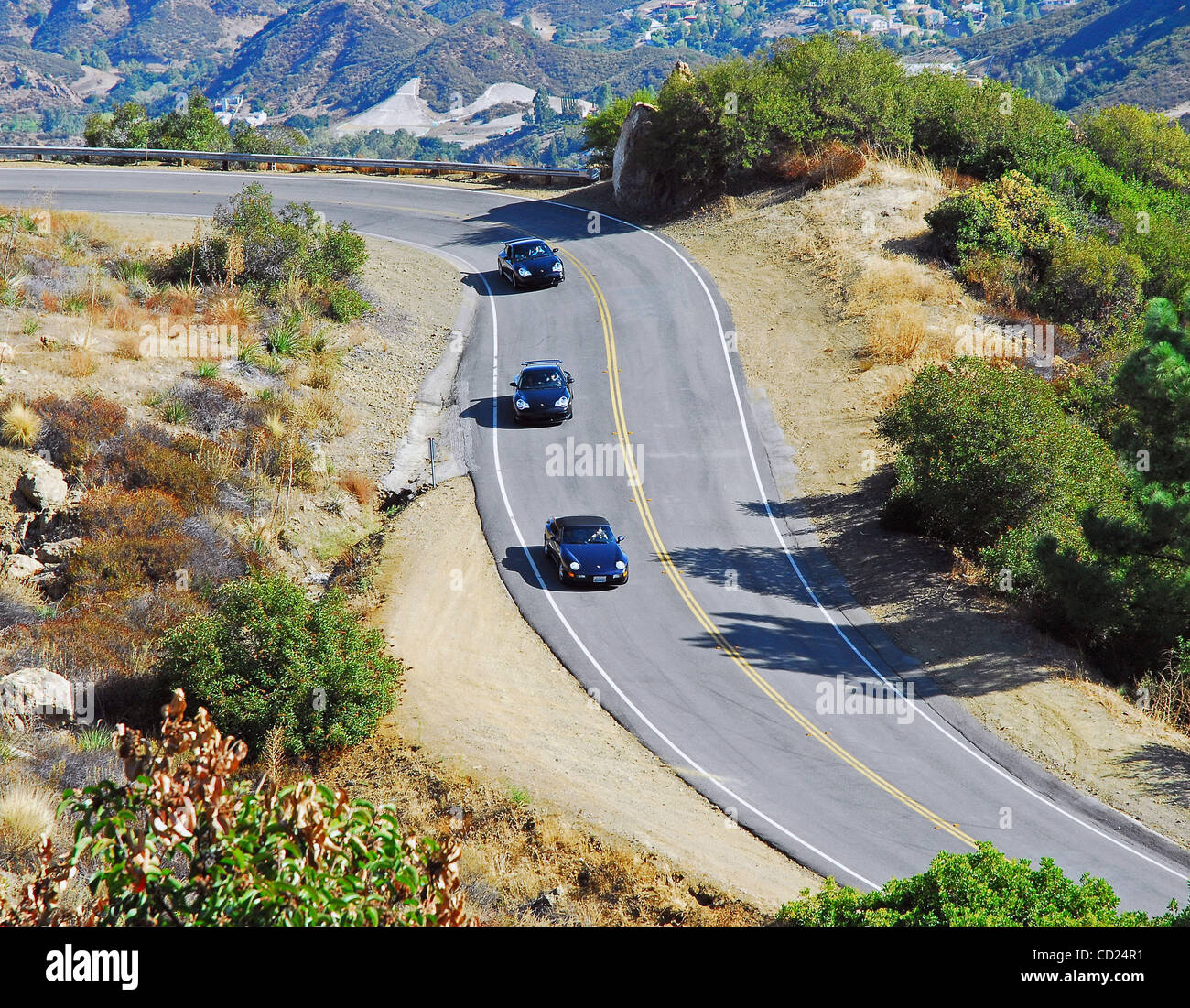Three Porsche 911's Racing Down A Hairpin Curve In The Mountains Stock Photo
