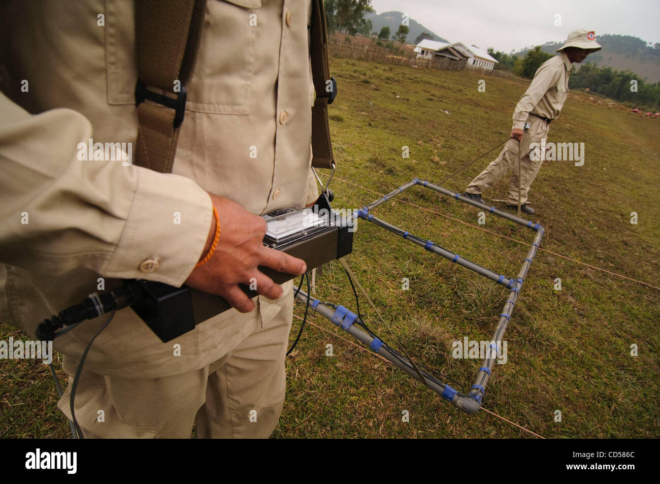 UXO Laos bomb disposal personnel using an Ebinger UPEX 740M metal detector  in a field full of un-expolded cluster ordnance. a few meters from the  field boundary is the local school. Xieng