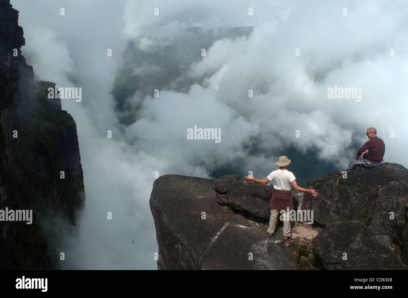 Apr 21, 2008 - Canaima, Venezuela - At and above cloud level, American Ben Ballweg, left, and Italian Roberto Aquila talk about the immense size of nearby Mount Canaima while sitting on rocks with a drop of hundreds of meters atop Mount Roraima, a 2,810-meter high mountain located in southern Venezu Stock Photo