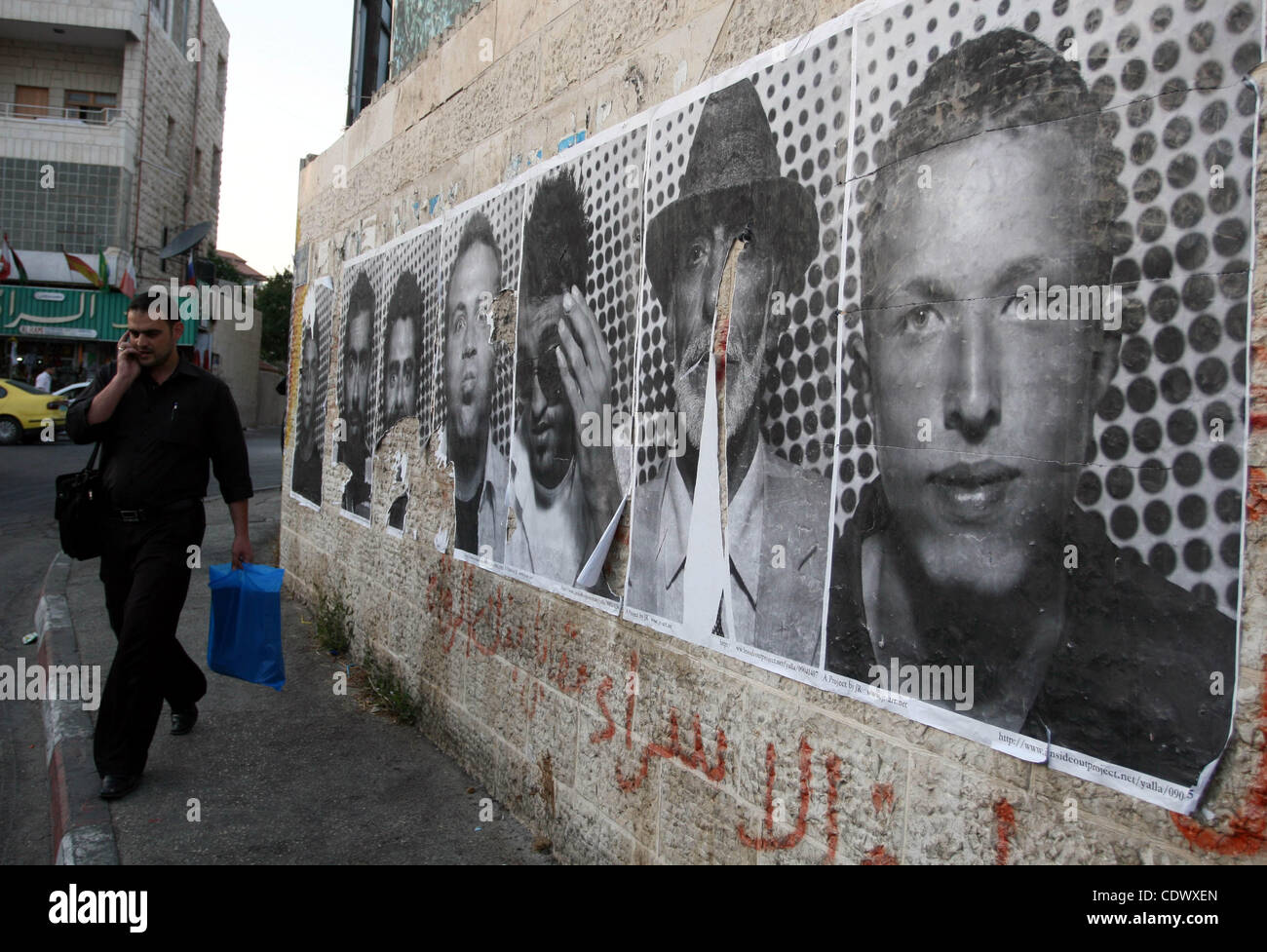A Palestinian man walks past large black and white photographs taken by French street artist JR of Palestinians, on September 6, 2011, in the West Bank city of Ramallah. JR's project entails having Palestinian and Israeli portraits taken which are then printed and pasted onto walls In Israel and the Stock Photo