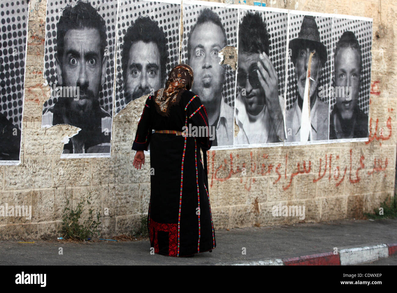 A Palestinian woman walks past large black and white photographs taken by French street artist JR of Palestinians, on September 6, 2011, in the West Bank city of Ramallah. JR's project entails having Palestinian and Israeli portraits taken which are then printed and pasted onto walls In Israel and t Stock Photo