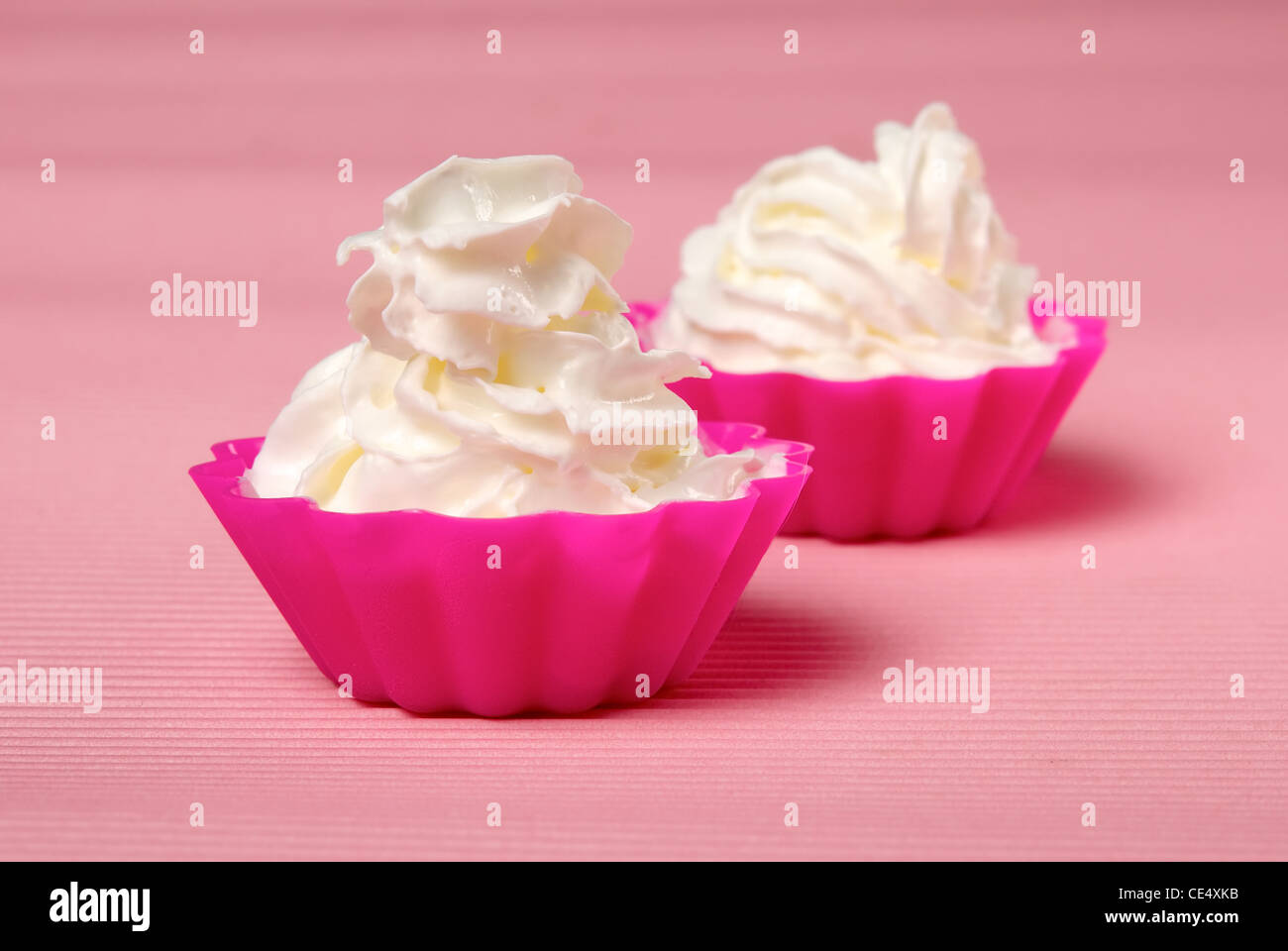 Two portions of whipped cream over pink background. Shallow DOF Stock Photo