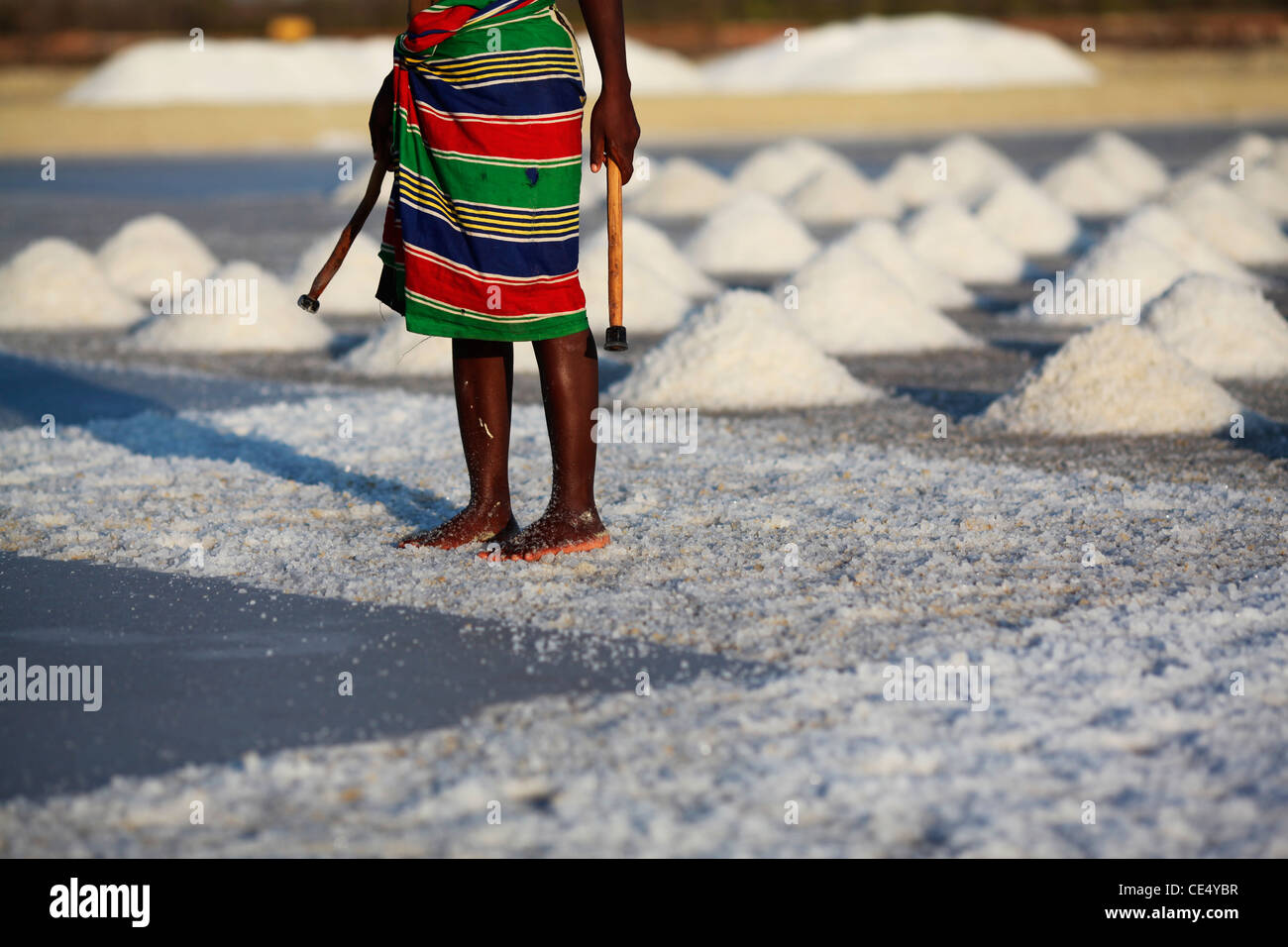 A malagasy  woman in a colourful skirt, breaking the salt crust, stands in the middle of the salt fields near Belo sur Mer Stock Photo