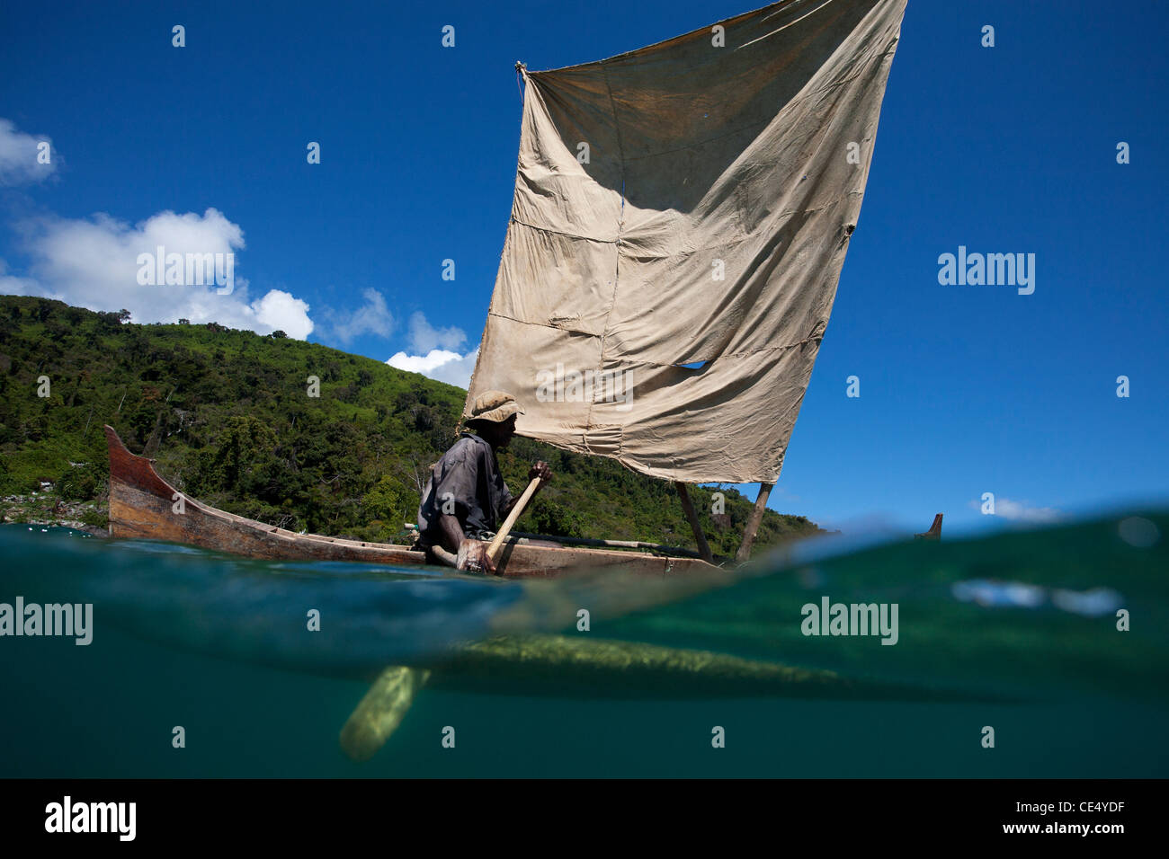 Split under over view of malagasy man rowing his pirogue, or outrigger dugout canoe. Nosy Komba, Madagascar, Africa. Stock Photo