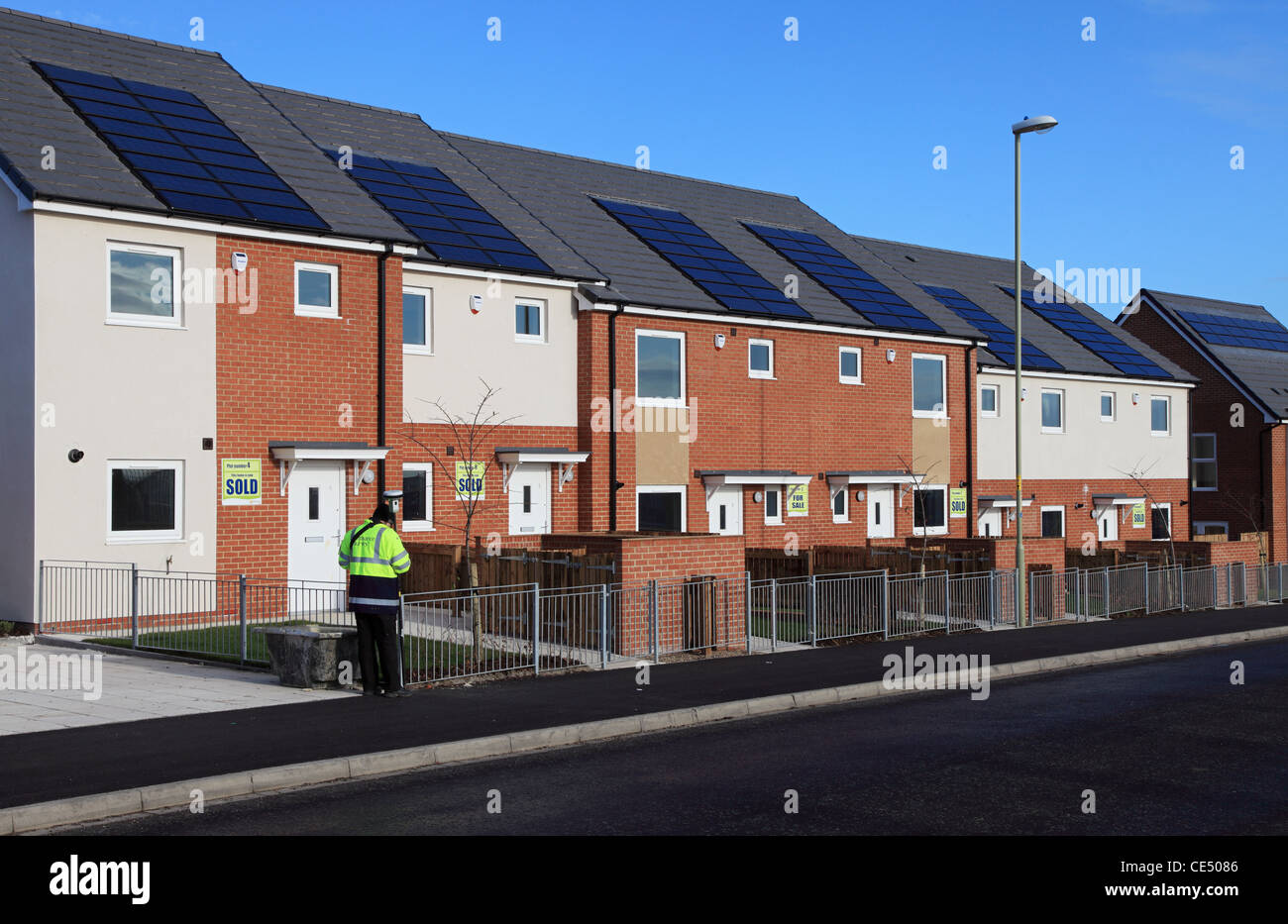 An Ordnance Survey surveyor measures the position of a street of new houses fitted with solar panels in Whitburn, north east England, UK Stock Photo