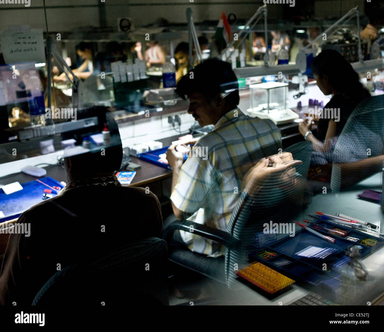 Supervisors inspect cut and polished diamonds a cutter/polisher is reflected in the glass. Stock Photo