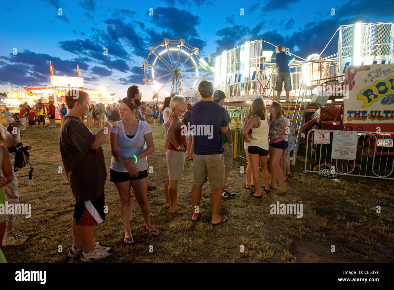 A line of people waiting for rides and lights in motion of ride at the ...
