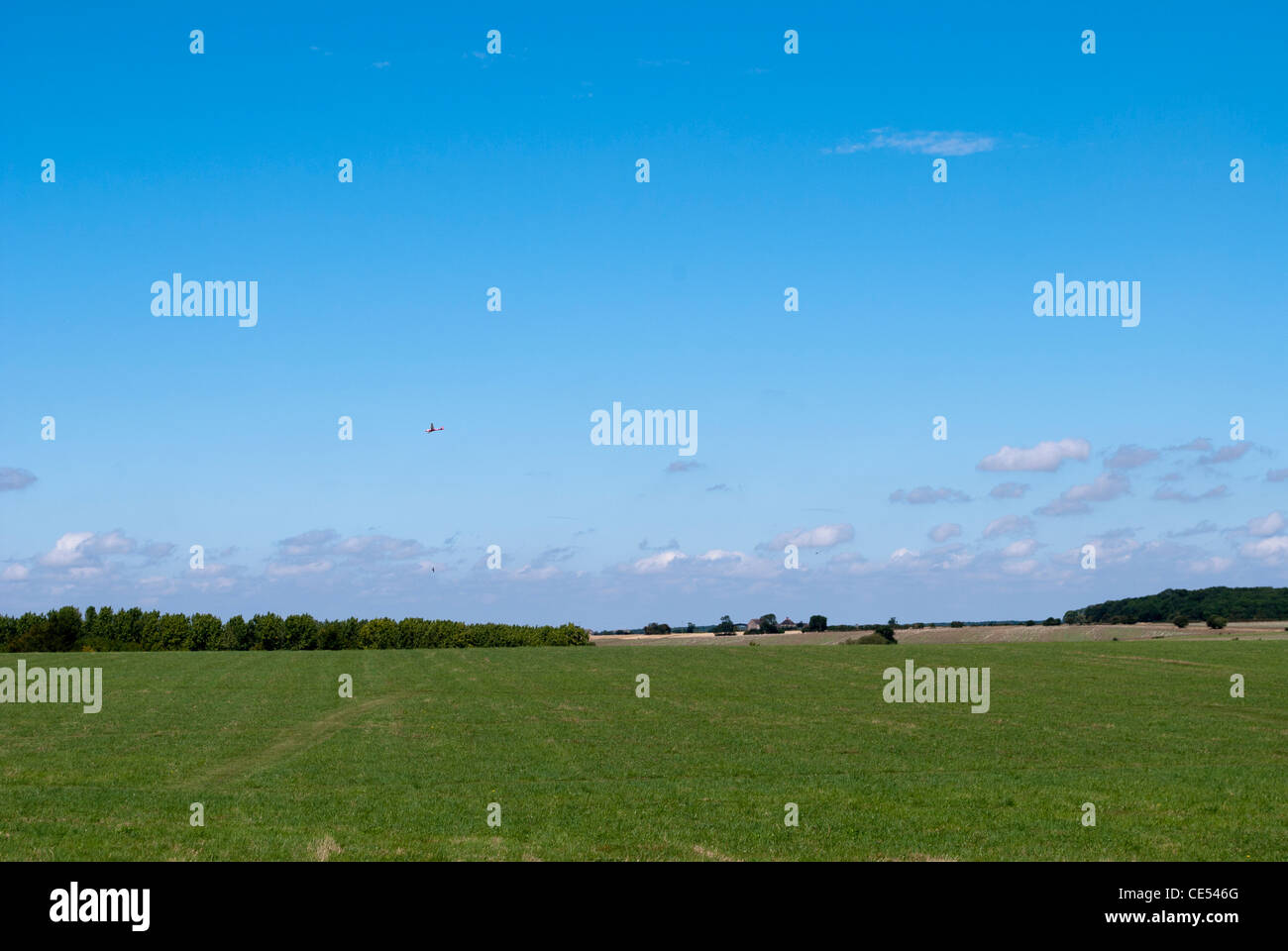 Glider In Blue Sky Flying Over Green Grass Field At Lyveden New Bield glider-in-blue-sky-flying-over-green-grass-field-at-lyveden-new-bield