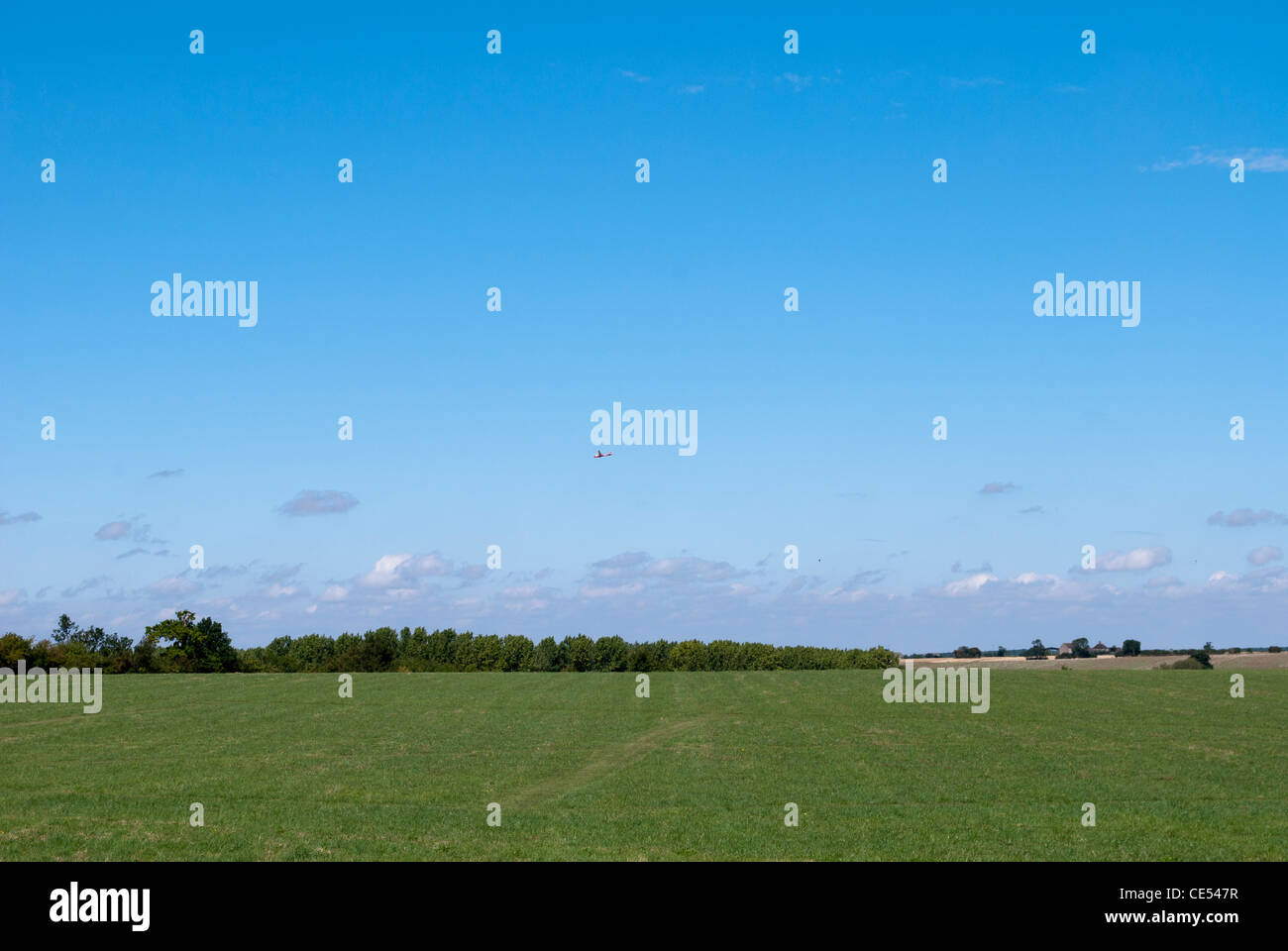 Glider In Blue Sky Flying Over Green Grass Field At Lyveden New Bield glider-in-blue-sky-flying-over-green-grass-field-at-lyveden-new-bield