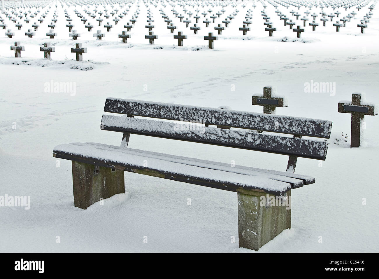 bench at graveyard surrounded with crosses and covered in snow war cemetery in winter military burial ground Stock Photo