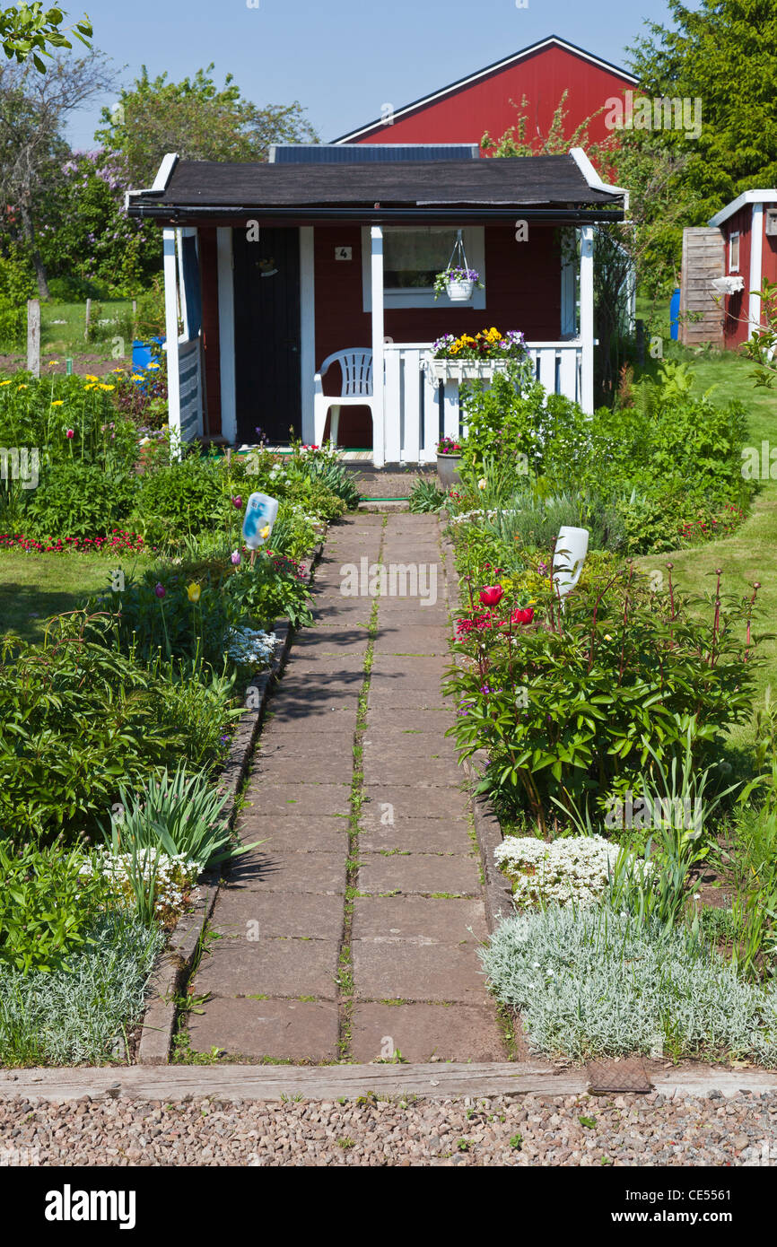 A small cottage on an allotment garden with flowers in the flower bed along the gravel path Stock Photo