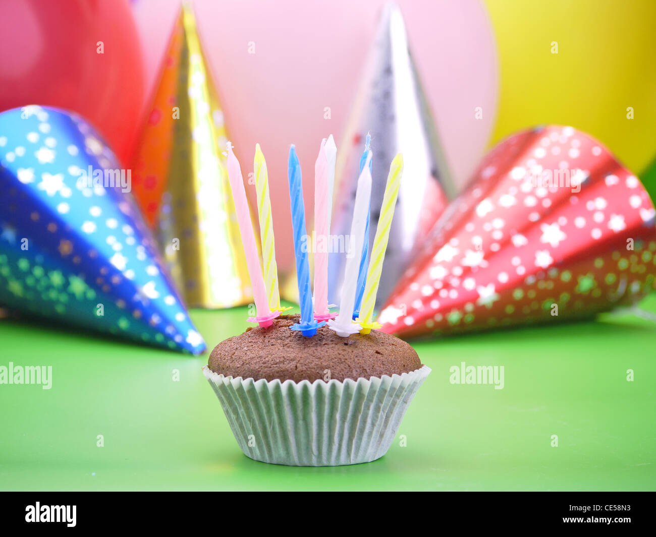 Chocolate muffin with eight candles with party cone caps and balloons in the background Stock Photo