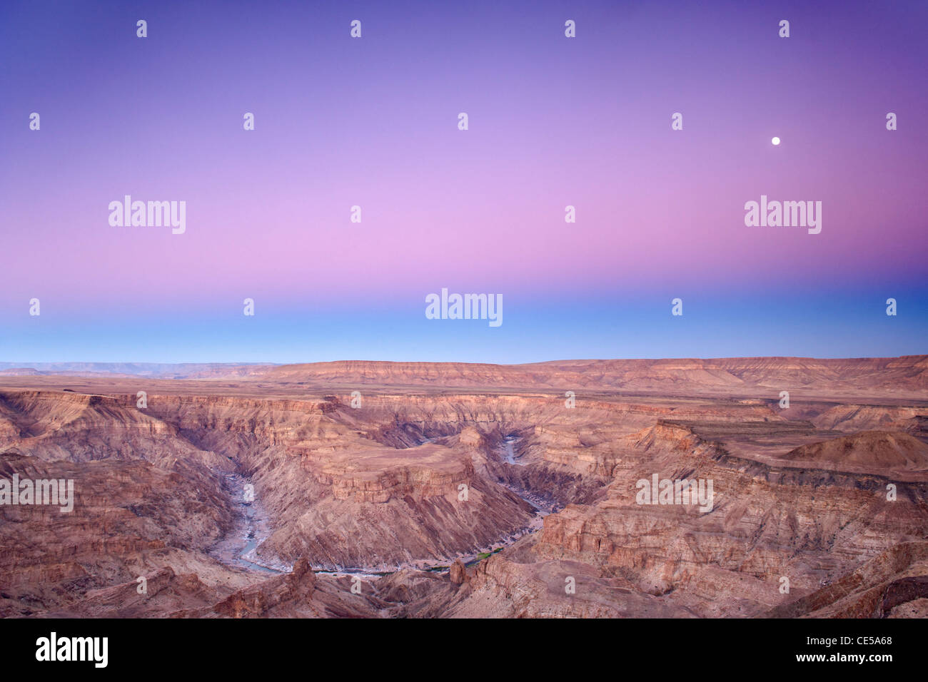 Full moon setting over the Fish River Canyon in southern Namibia at dawn. Stock Photo