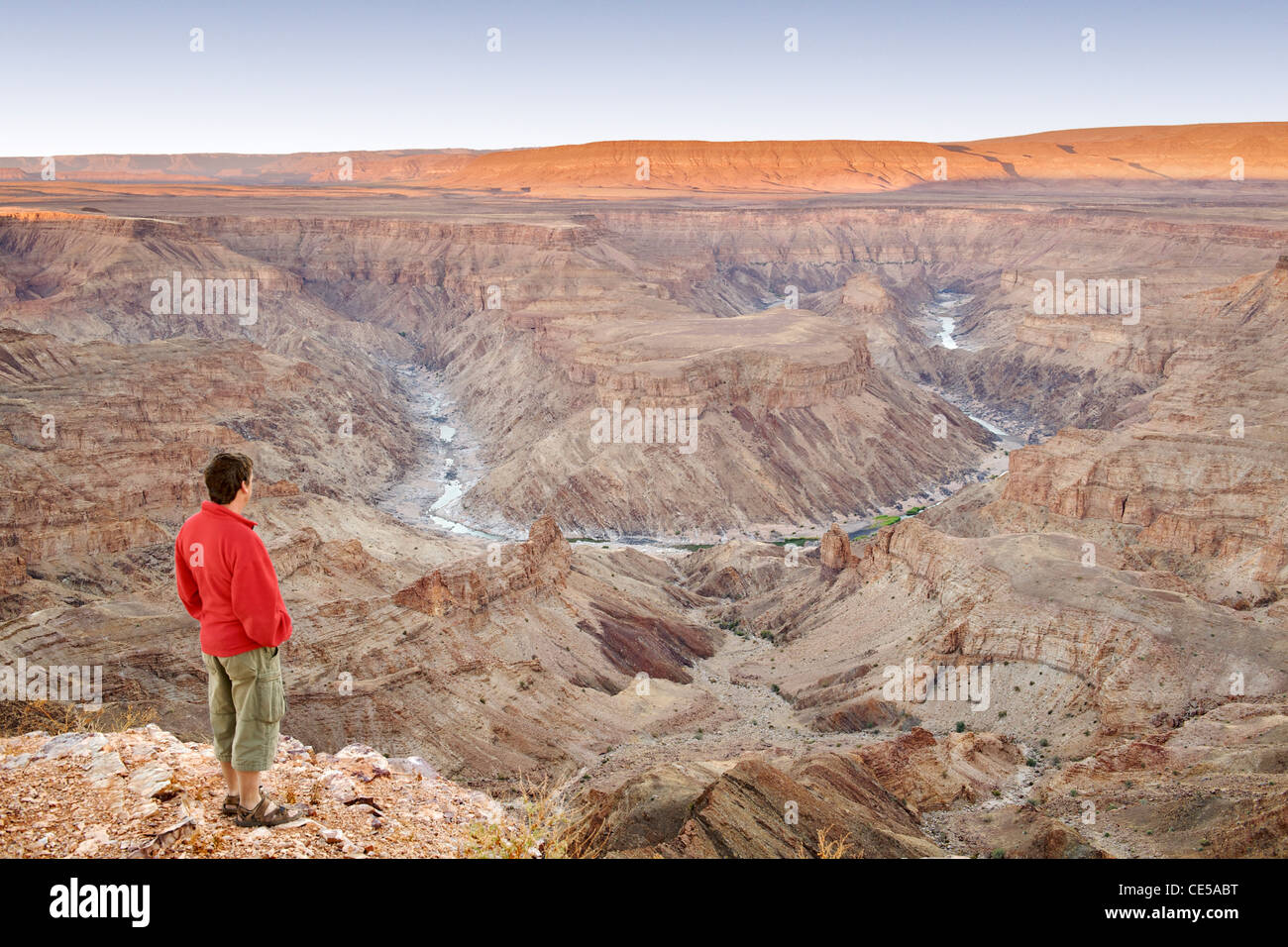 A man stands looking out across the Fish River Canyon in southern Namibia at dawn. Stock Photo
