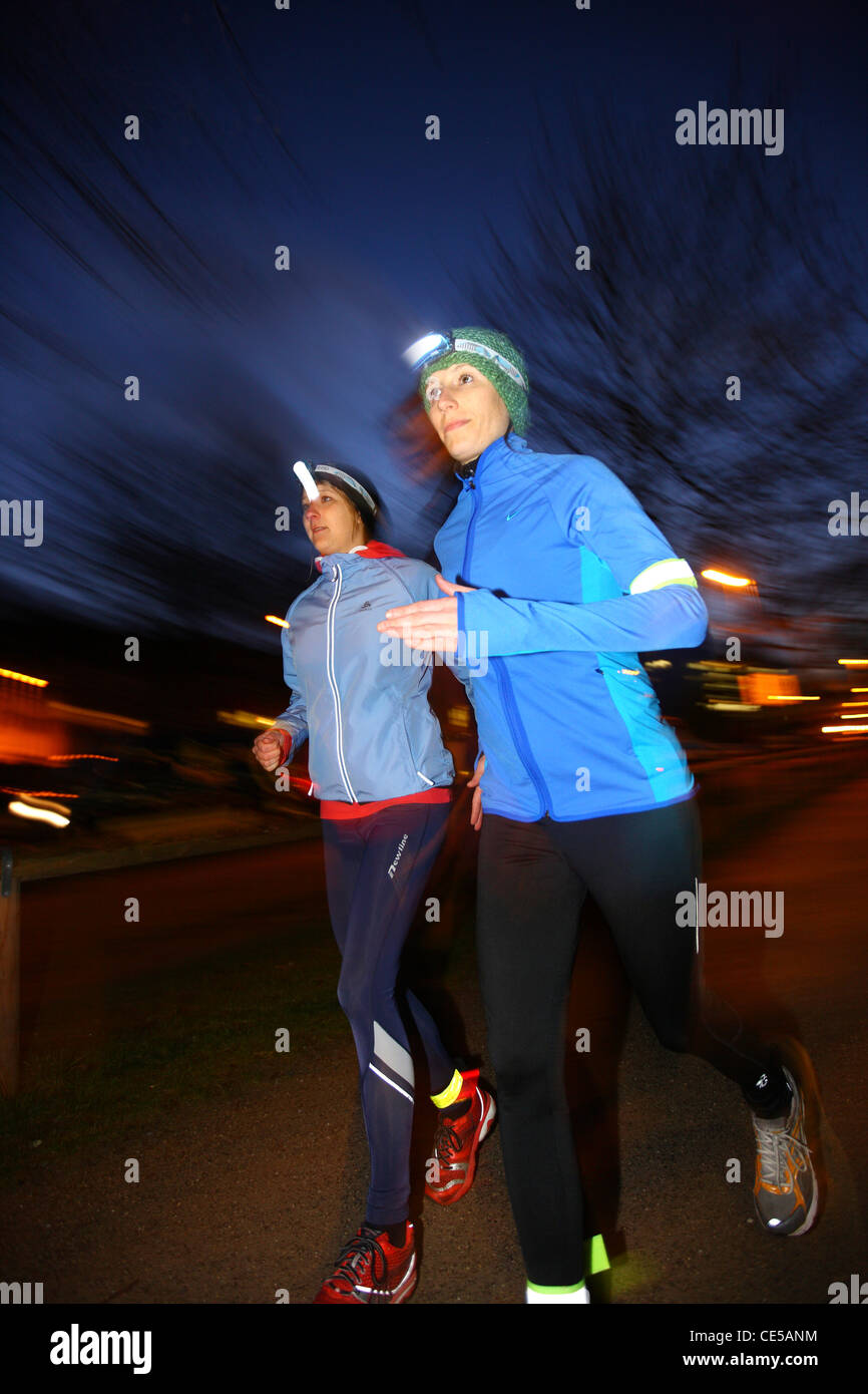 Two young women jogging at night in winter, fall. With headlamps in the