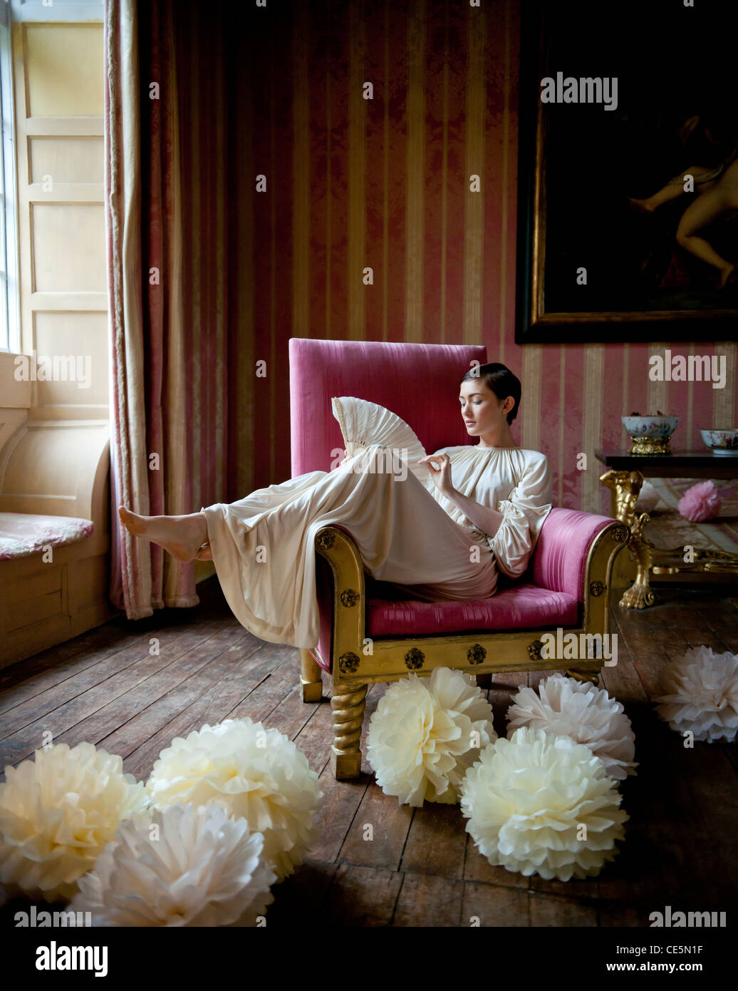 A woman sitting on a chair, holding a fan Stock Photo