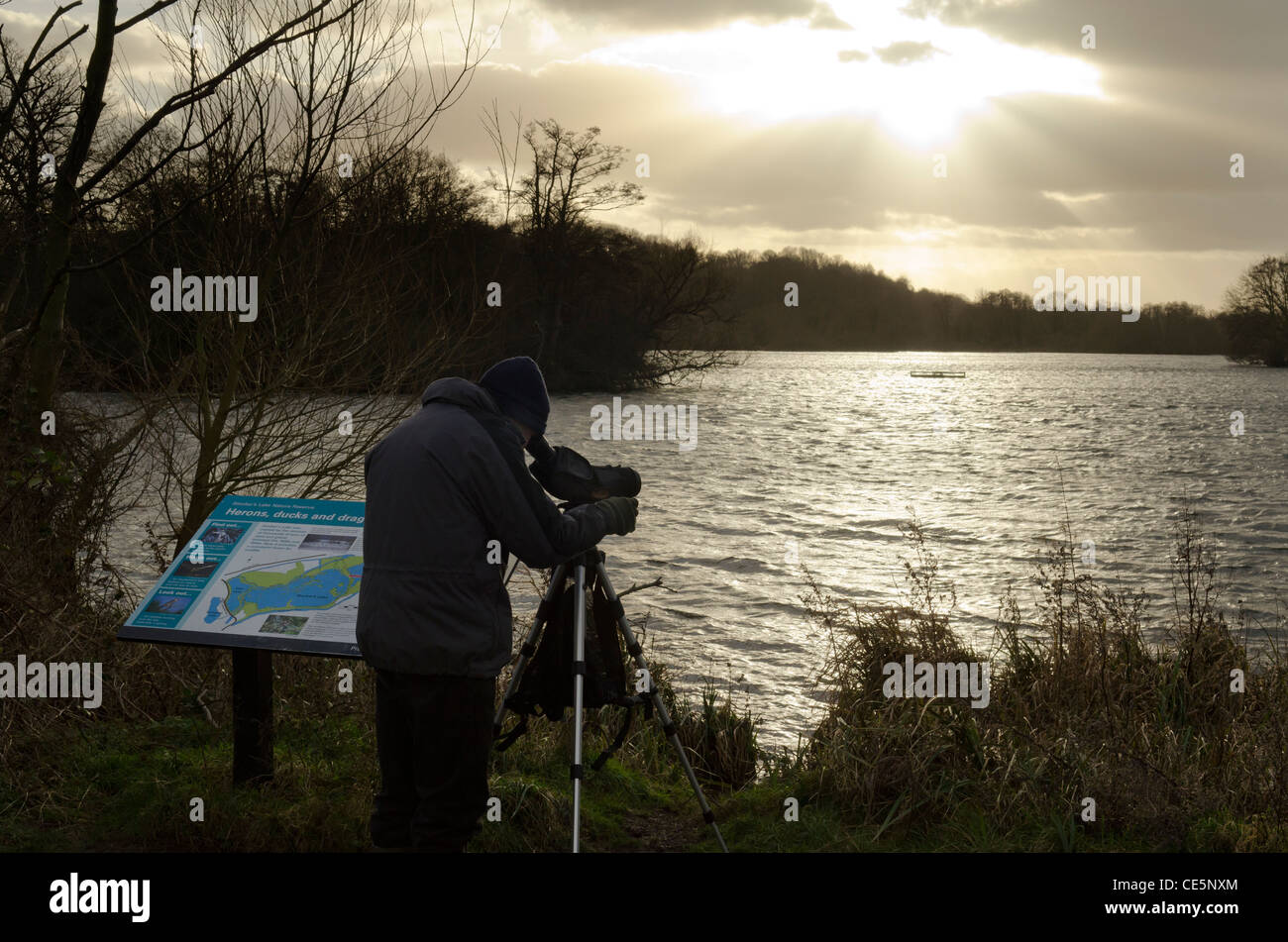 A silhouette of a bird watcher using a telescope by Stockers Lake in Winter near Rickmansworth Herts UK Stock Photo