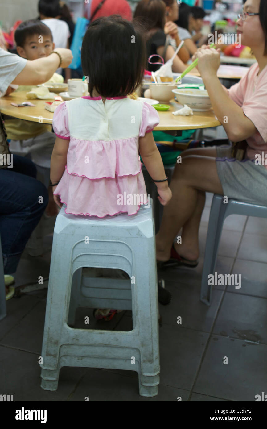Little girl seat on a stack of plastic benches in a Kuala Lumpur restaurant Stock Photo