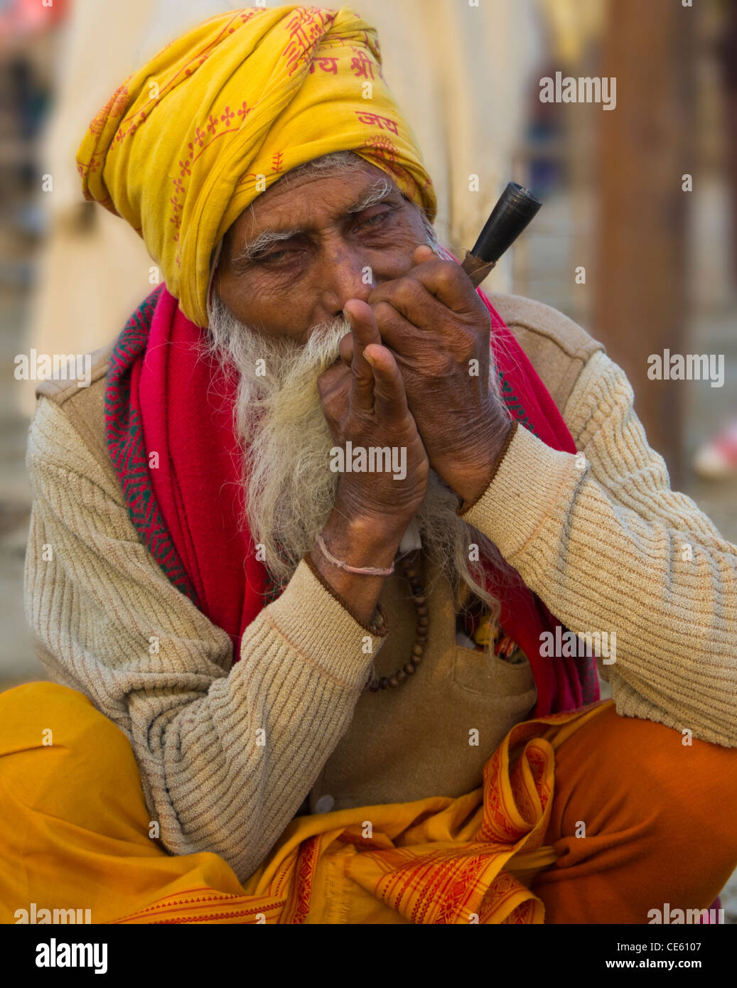 elderly pilgrim in saffron clothes and white beard smoking chillum