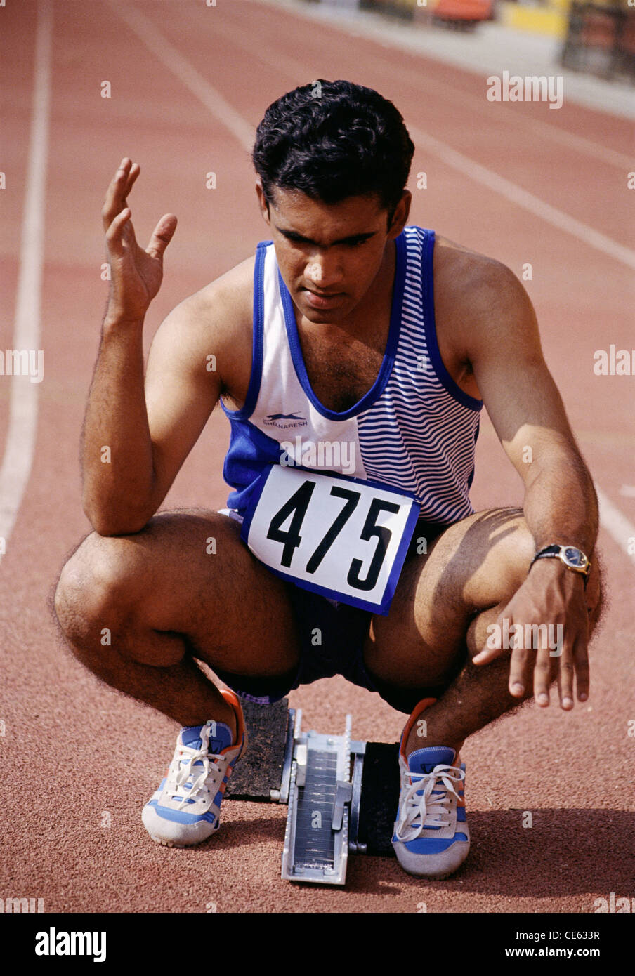Indian teenager boy athlete runner at sprint starting block on race track ; India ; Asia ; Asian