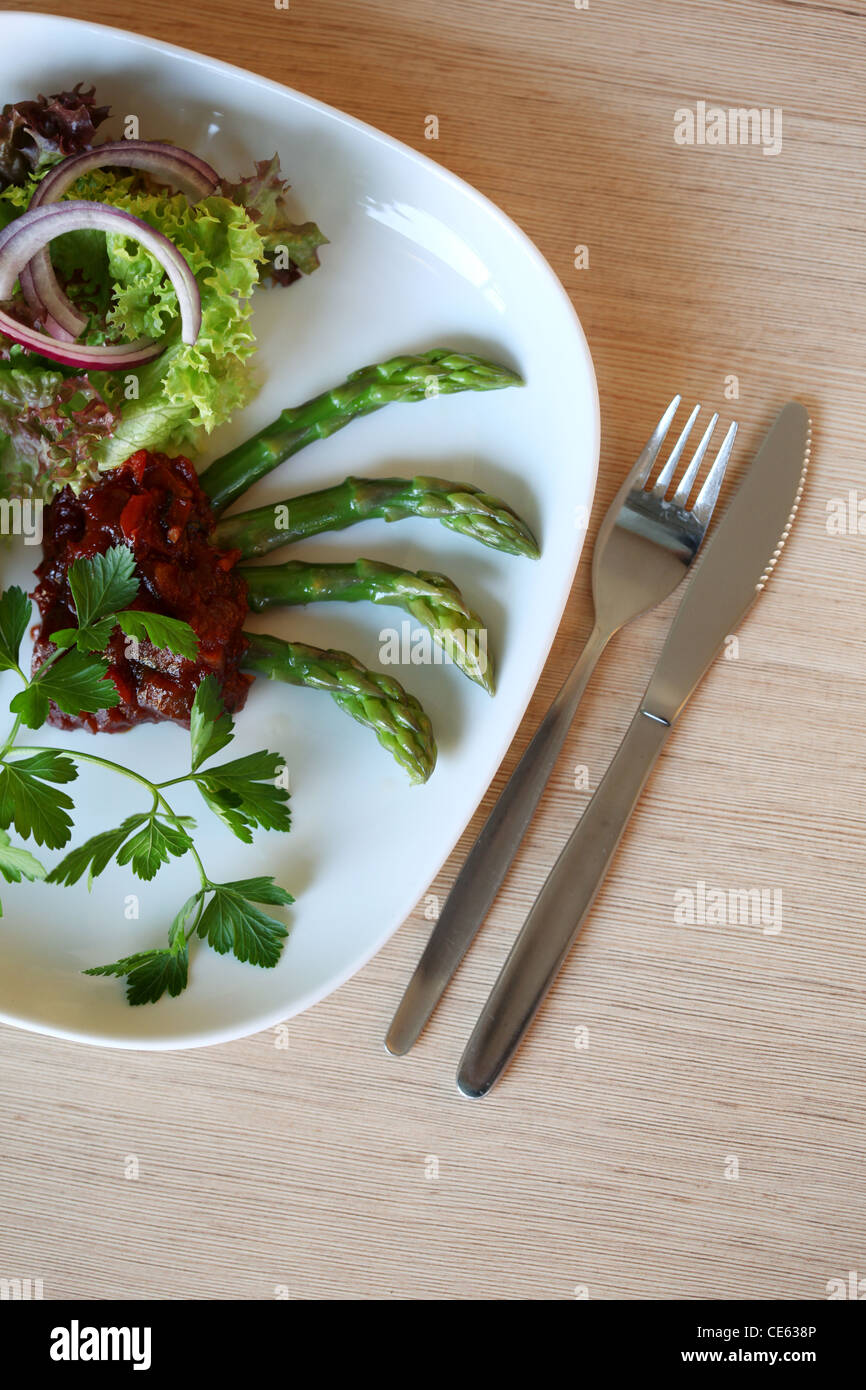 Arranged plate with green salad, onions, parsley and asparagus with spicy red sauce served in a restaurant Stock Photo