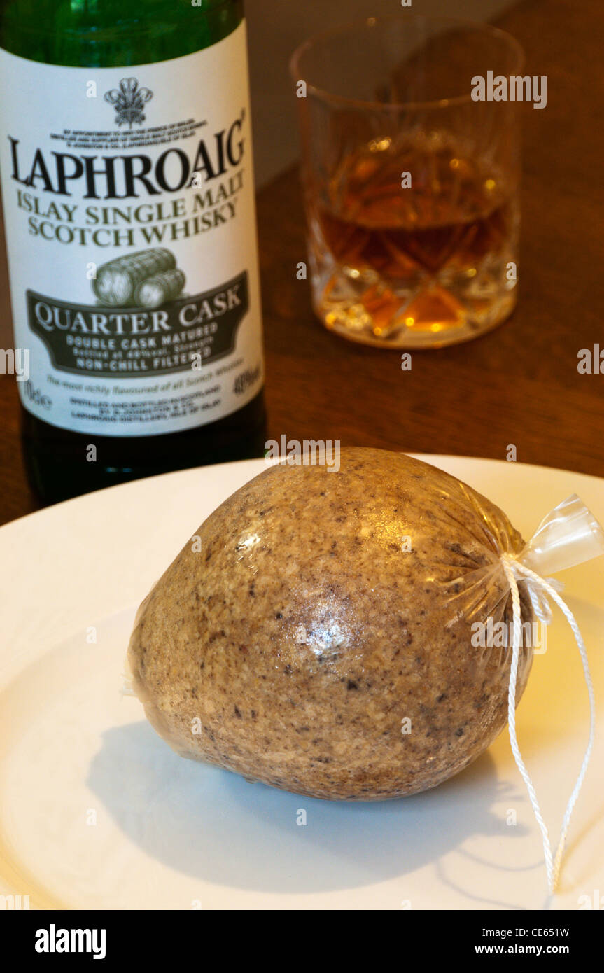 A haggis on a plate in front of a bottle of Laphroaig malt whisky and a glass of whisky. Stock Photo