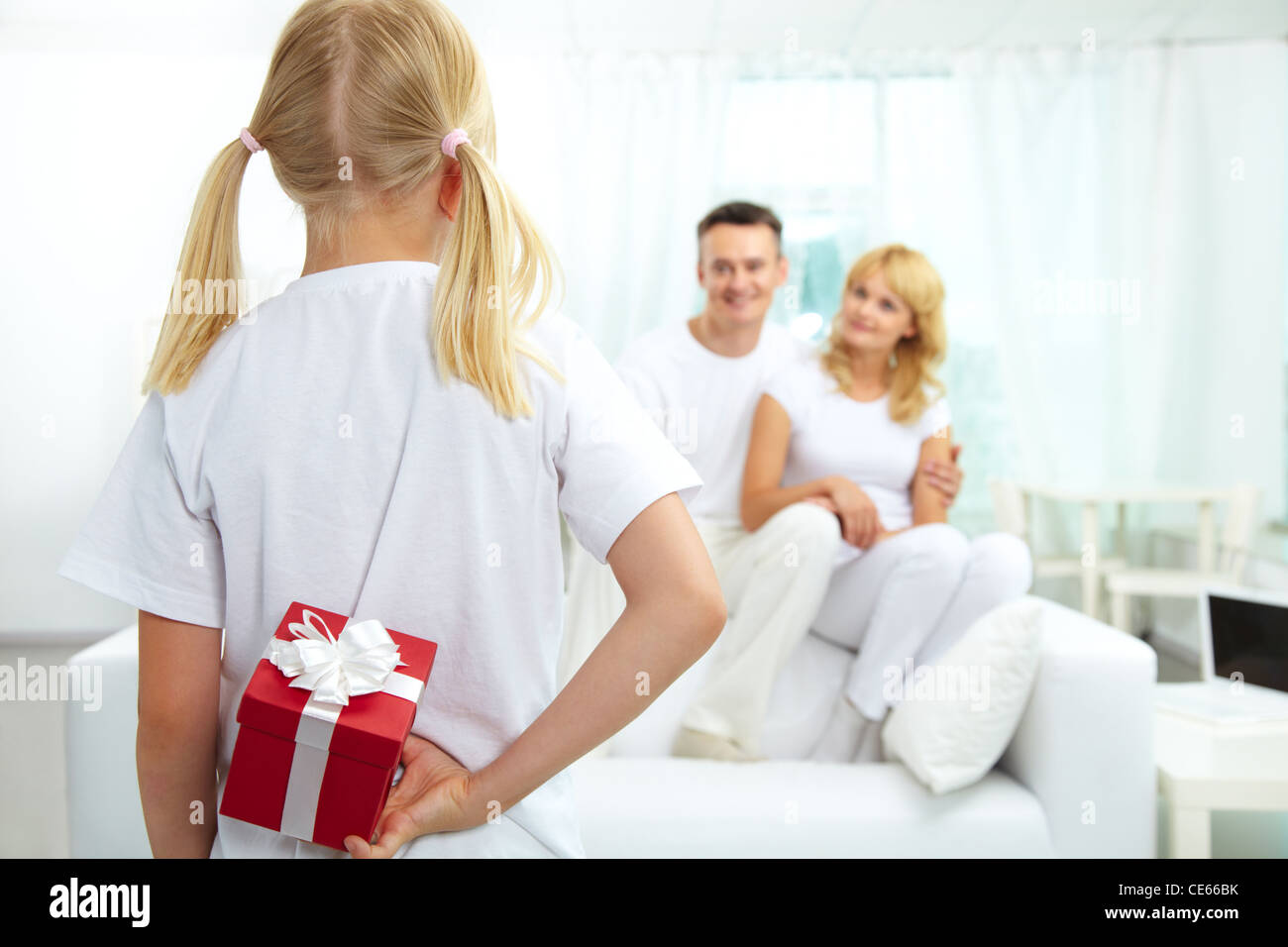 Back view of daughter hiding giftbox while looking at her parents Stock Photo