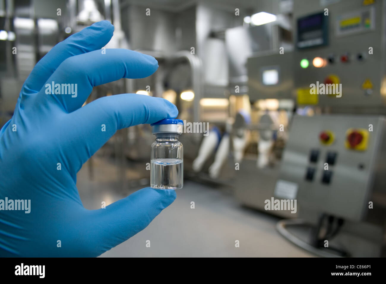 Hand in rubber glove holding a bottle of medicine against the background of the production line drugs Stock Photo