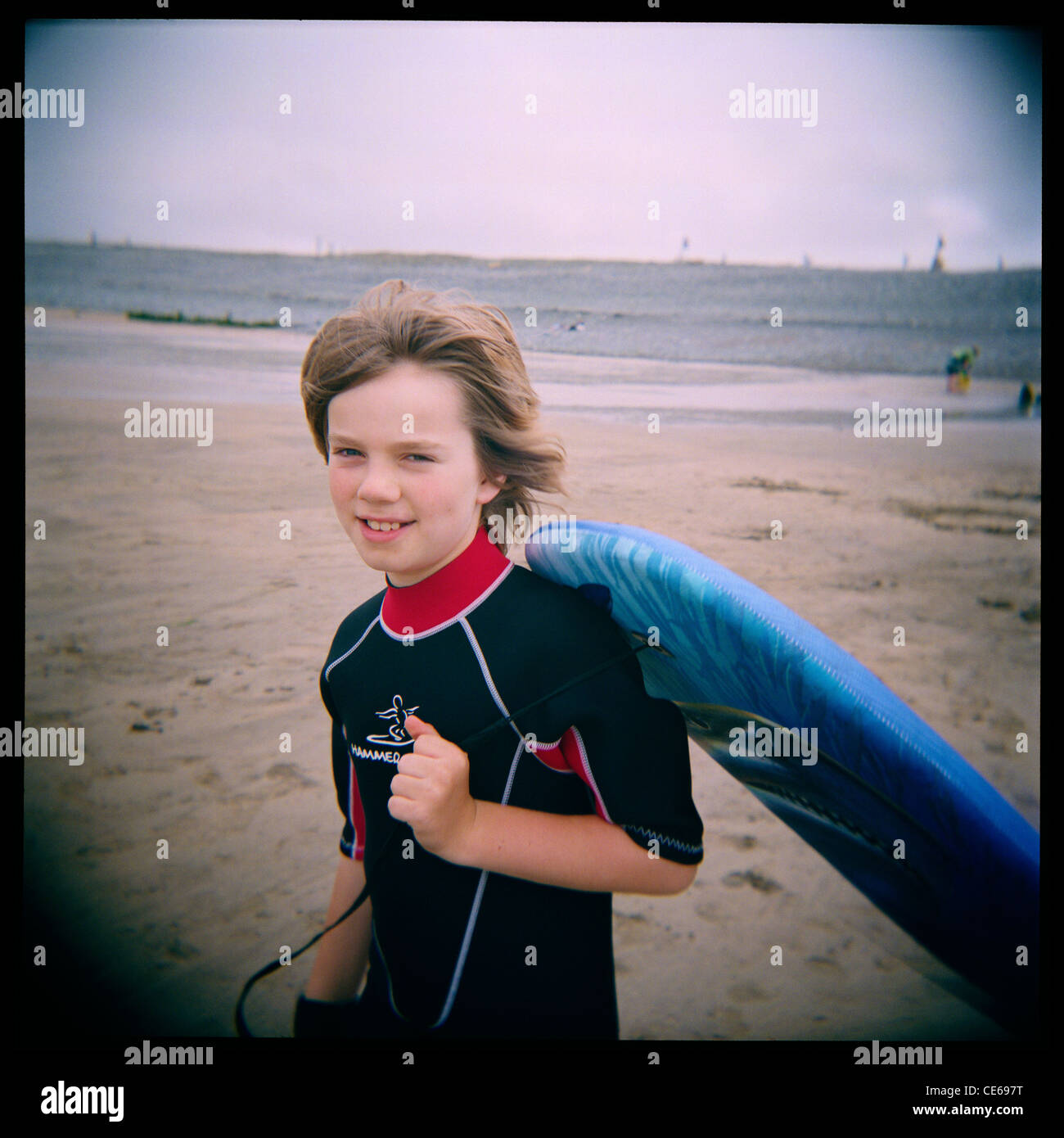 10 year old boy carrying a body-board on the beach at Westward Ho!, Devon, England. Taken with a Holga medium format toy camera. Stock Photo