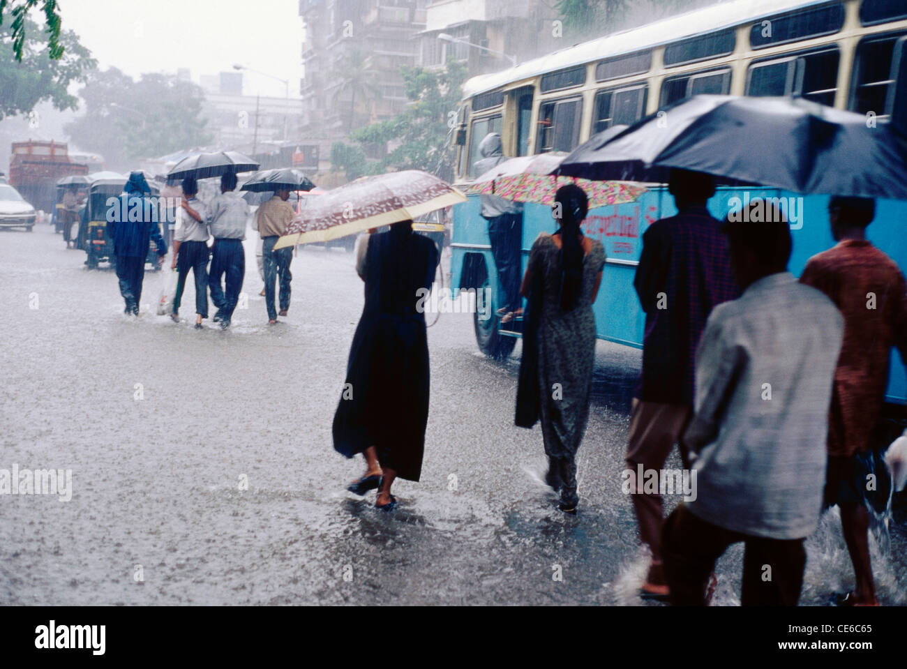 people with umbrellas walking in monsoon rain on flooded road ; bombay ...