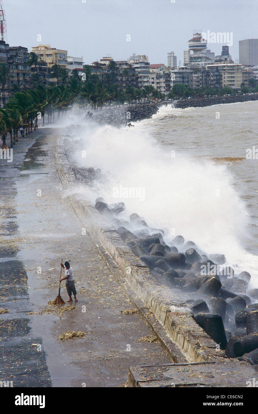 sweeper cleaning debris thrown by sea waves in monsoon on marine drive ; bombay mumbai ; maharashtra ; india Stock Photo