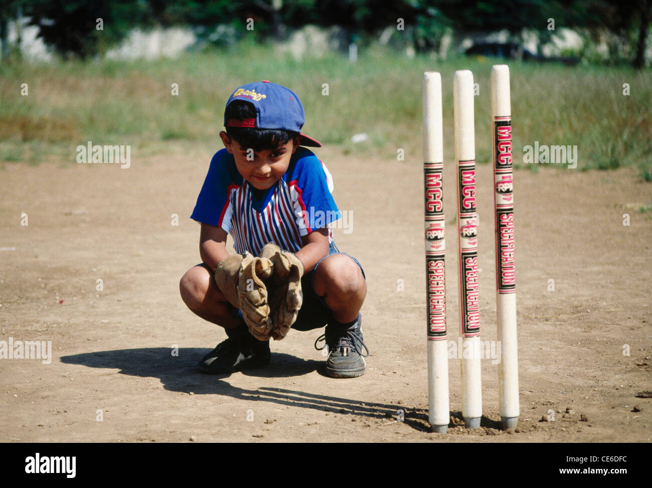 Indian child boy playing cricket doing wicket keeping sitting behind