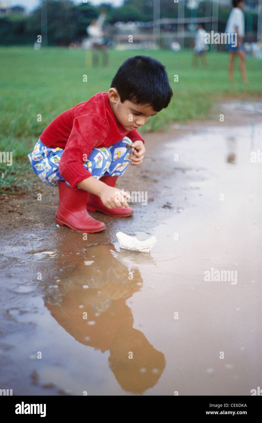 boy floating playing with paper boat in water puddle   Model Released Stock Photo