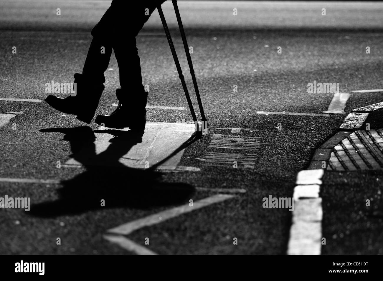 The legs of a man on crutches as he crosses a road at a zebra crossing Stock Photo