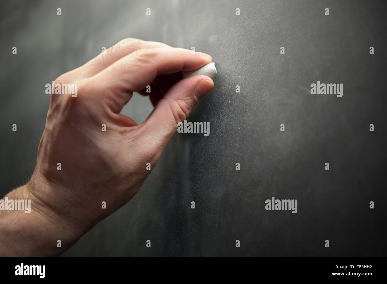 A man male teacher left hand writes using chalk on a chalkboard blackboard. Stock Photo