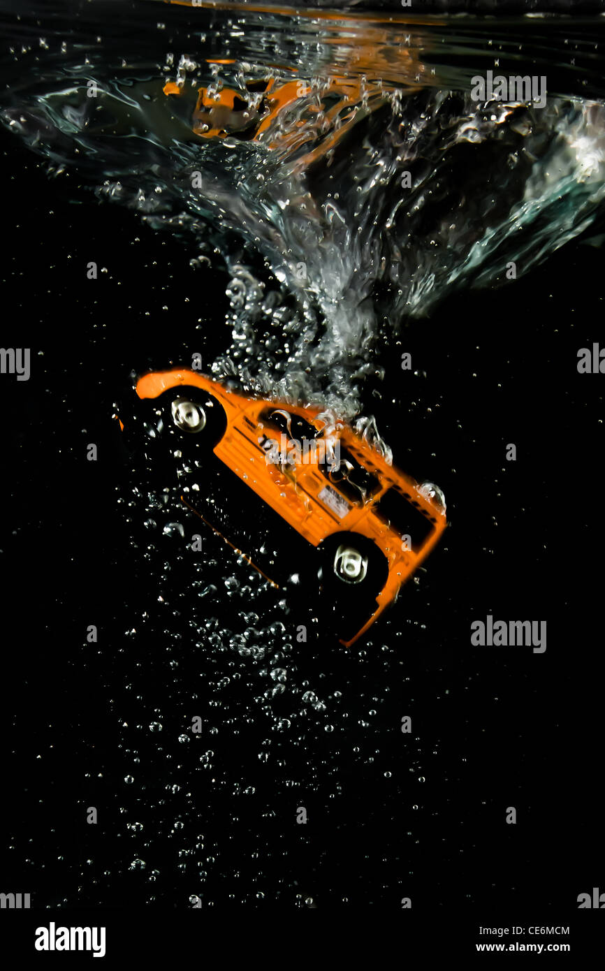 The moment of immersion for an orange Taxi cab, bubbles, speed, reflections on the liquid surface and swirl in a black backgroun Stock Photo