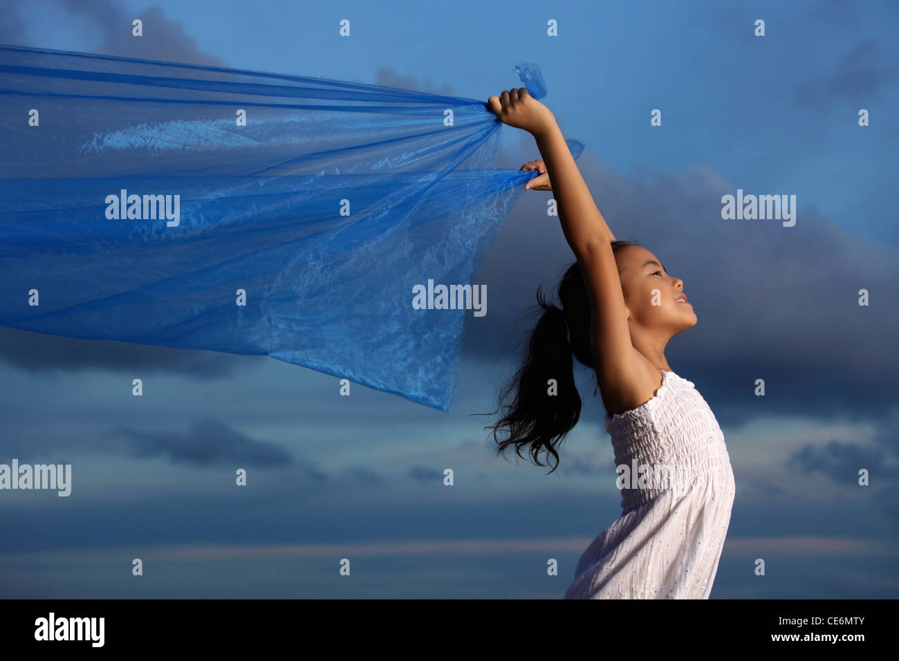 young girl holding up blue cloth, blue sky background Stock Photo