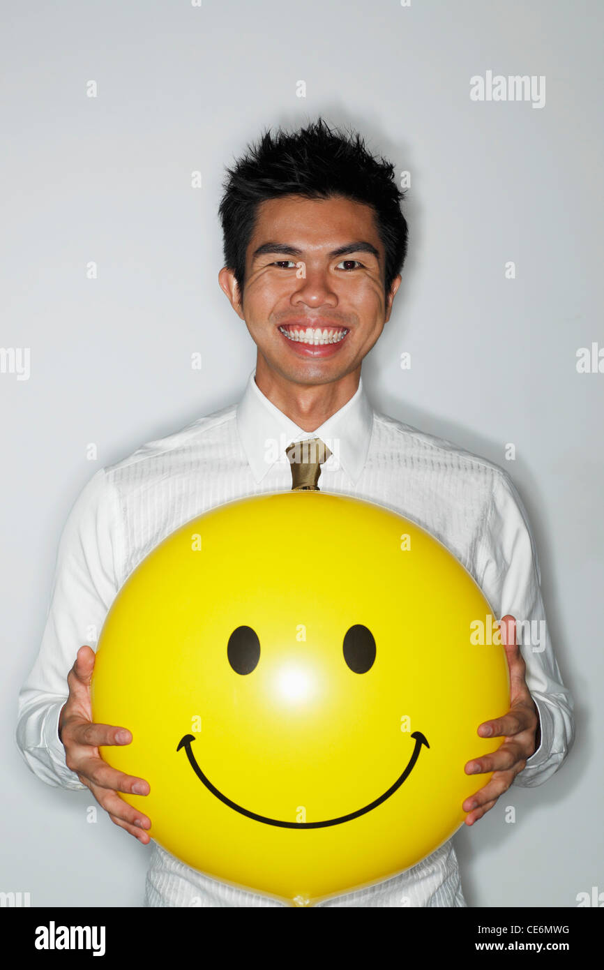 young man holding a big smiley face balloon and smiling Stock Photo