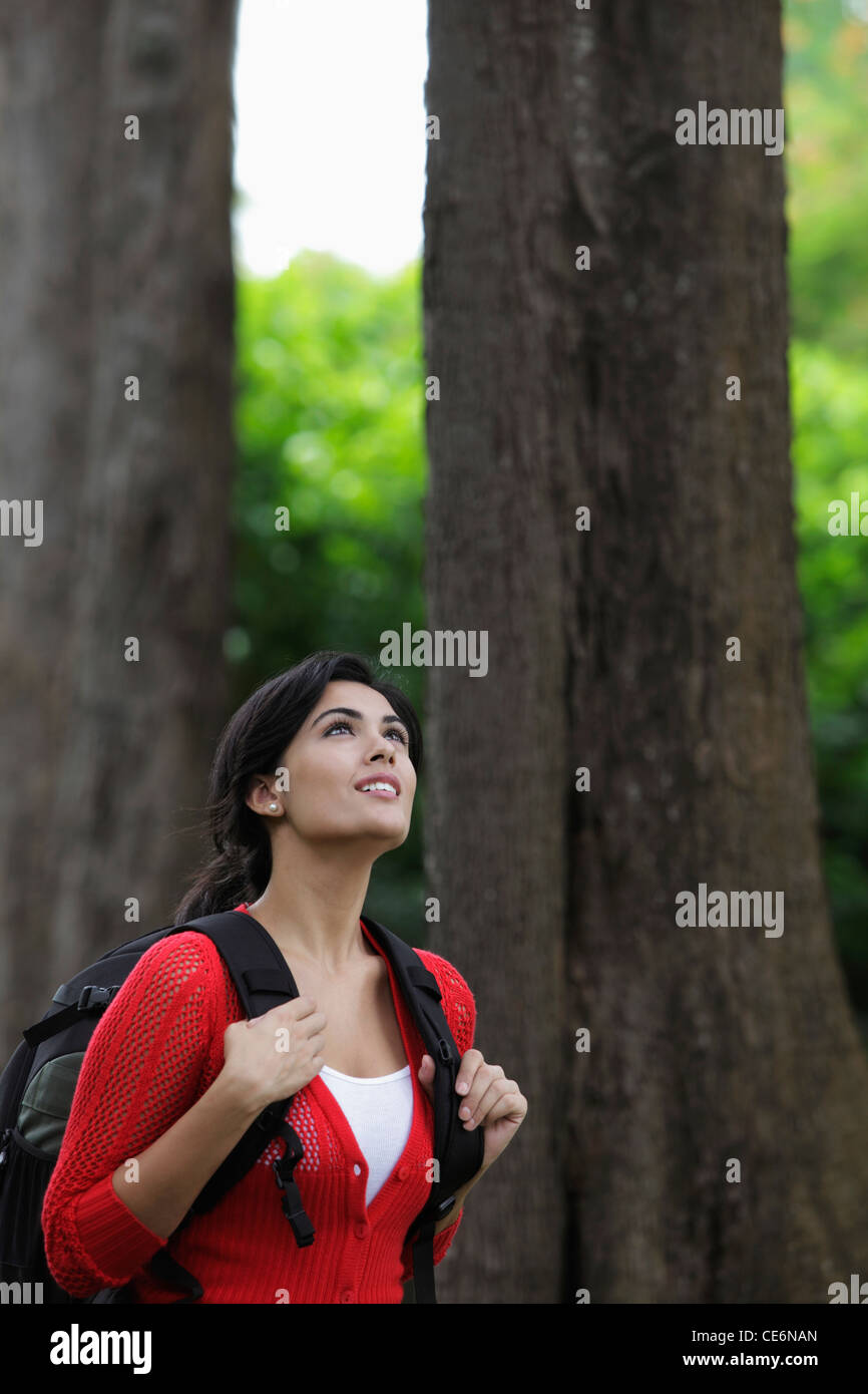 Mid shot of woman wearing back pack and looking up at trees. Stock Photo