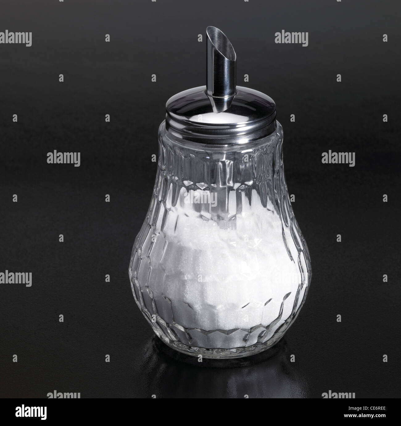 Studio photography of a sugar sprinkler made of glass and metal in dark reflective back Stock Photo