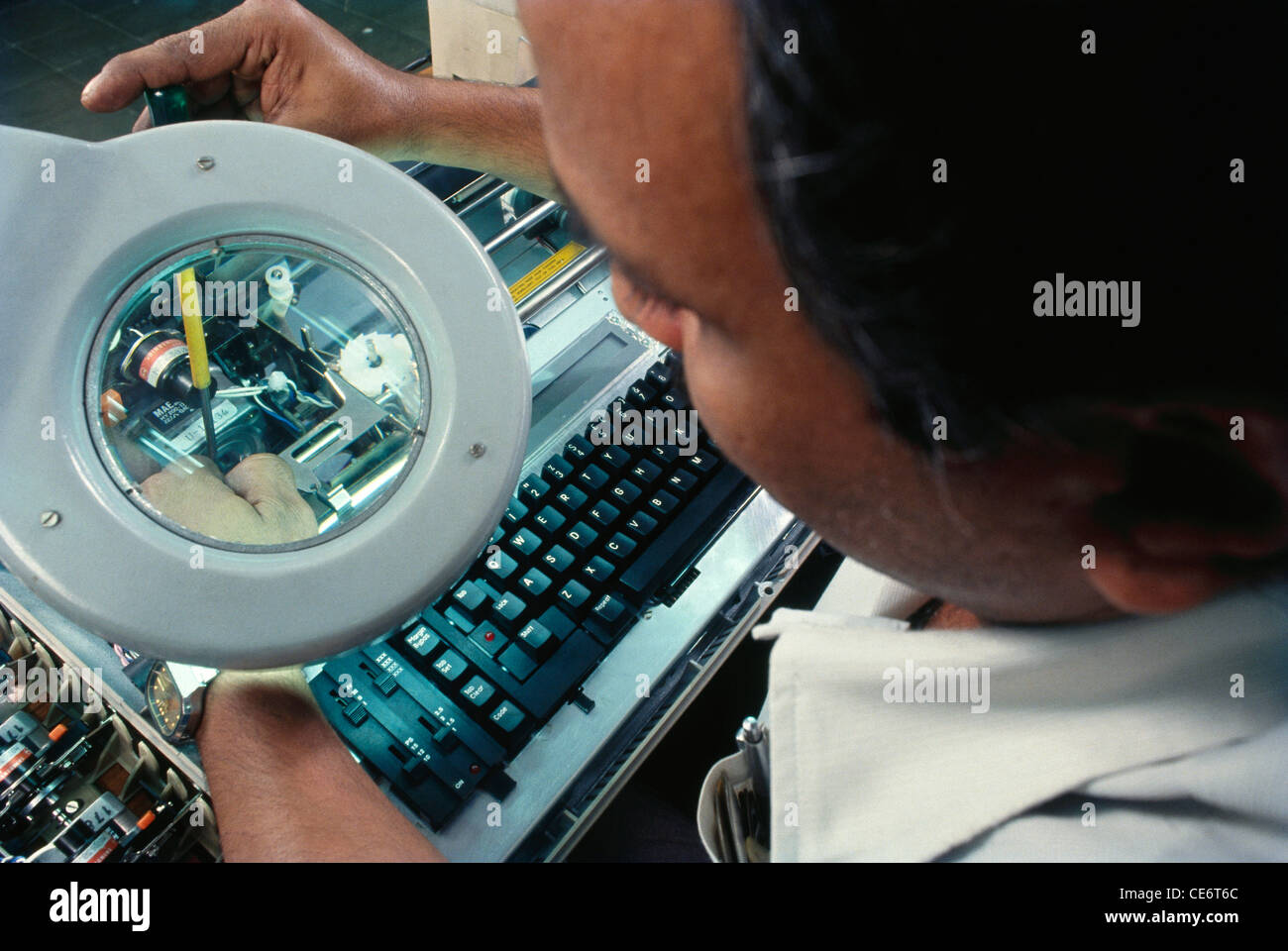 typewriter manufacture tightening screw looking through magnifying glass in factory ; india ; asia Stock Photo