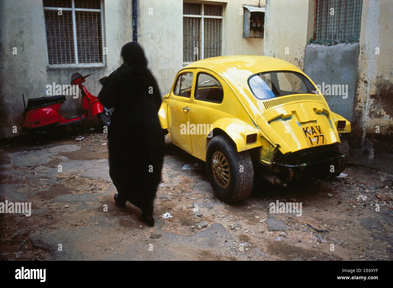 red scooter yellow vw volkswagen beetle vehicle parked car and women black burqa dress Mombasa Kenya Africa Stock Photo