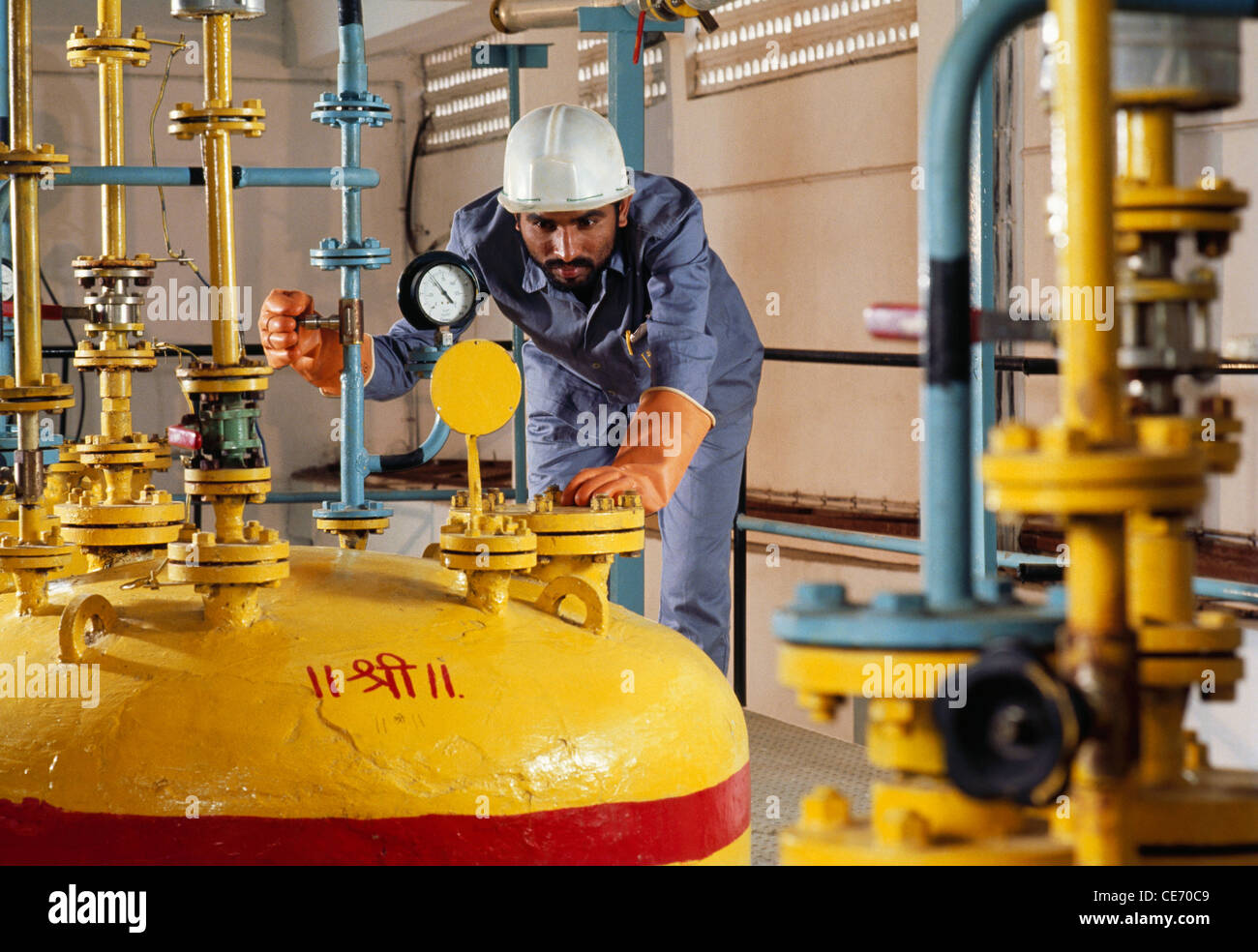 Indian man worker wearing helmet working in chemical factory ; auspicious Shree in Hindi written in red on yellow tank ; india ; asia Stock Photo
