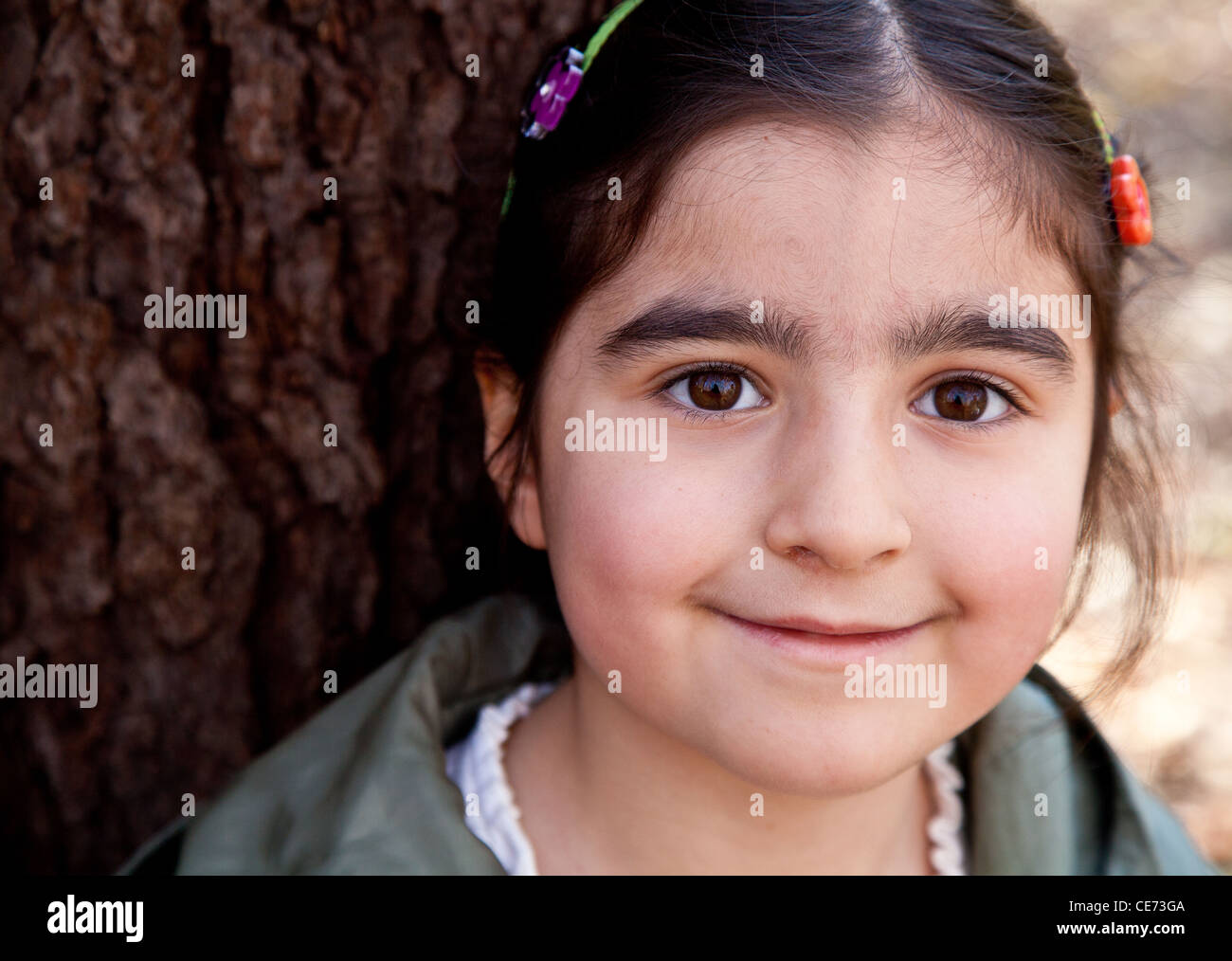 Closeup portrait of a smiling happy little girl in front of a tree with ...