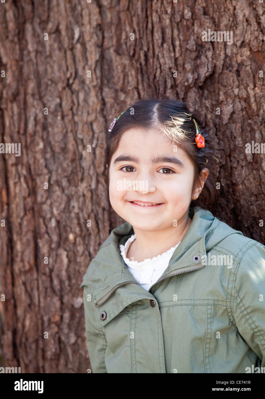Portrait of a smiling happy little girl in front of a tree with bark ...