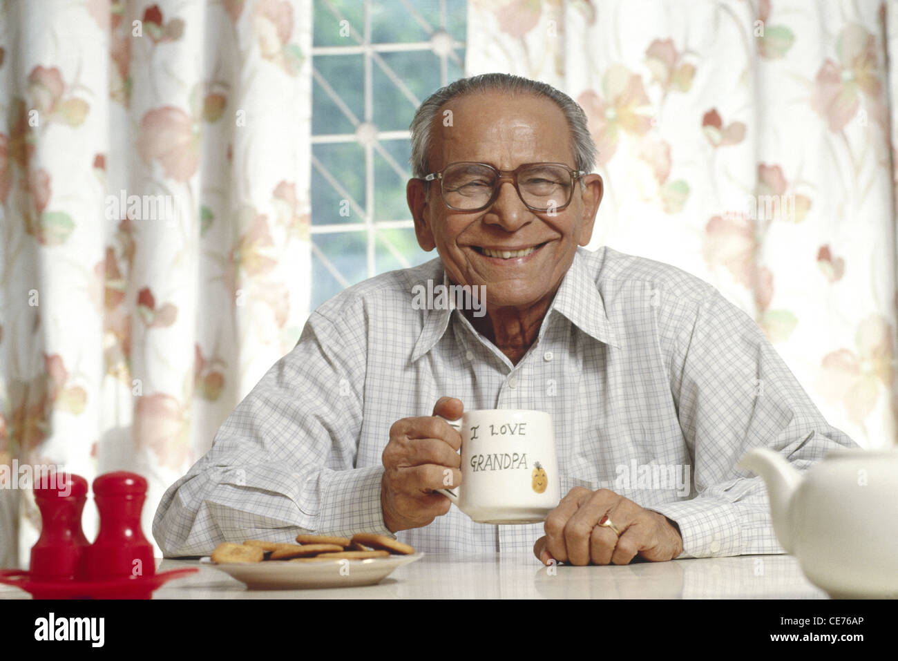 Indian senior old man holding cup of tea and biscuits in a saucer