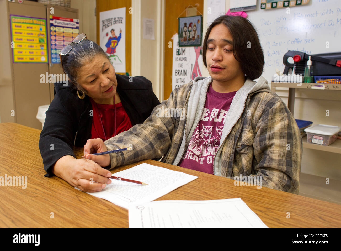 Hispanic female teacher in class works one-on-one with autistic teenage ...