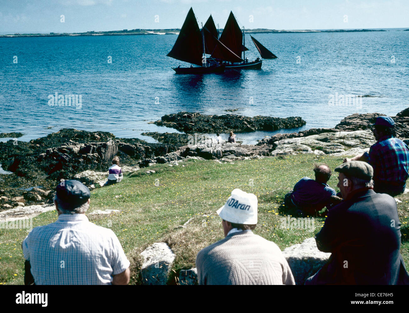 Men on a grassy bank watch a race in progress during the annual regatta  at Carna Connemera Co Galway  Ireland. Stock Photo